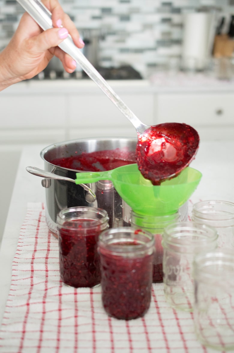 pouring homemade low sugar raspberry jam into Mason jars