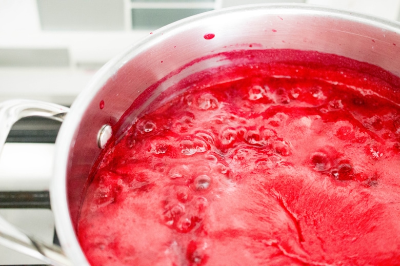 Homemade low sugar raspberry jam cooks at a rolling boil.