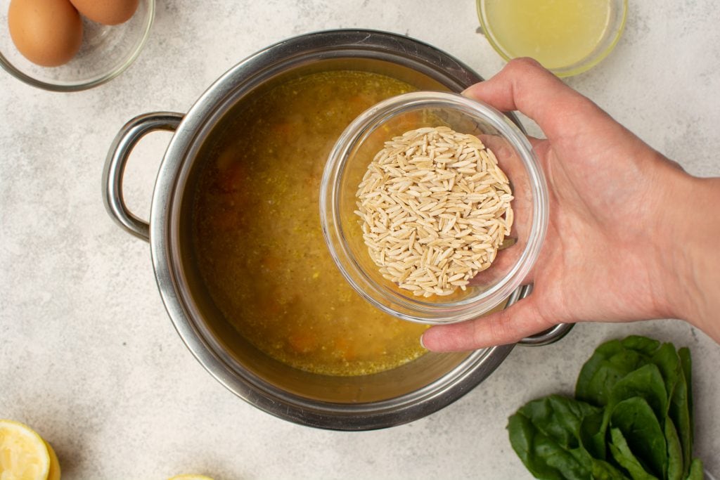adding whole wheat orzo to a pot of greek lemon soup with chicken