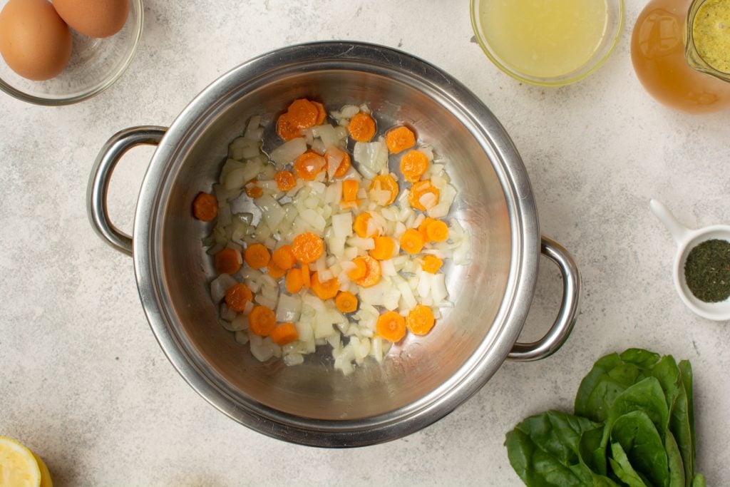 sauteing chopped carrots and onions in a large soup pot for chicken orzo soup