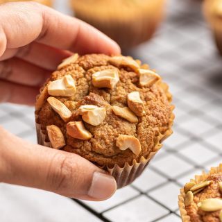 almond flour banana muffin held in a hand with cashews on top