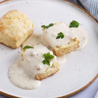 white plate with a vegan biscuit covered in white gravy