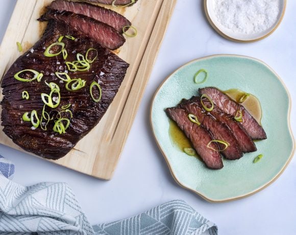 sous vide flank steak sliced on a wooden cutting board with sliced scallions