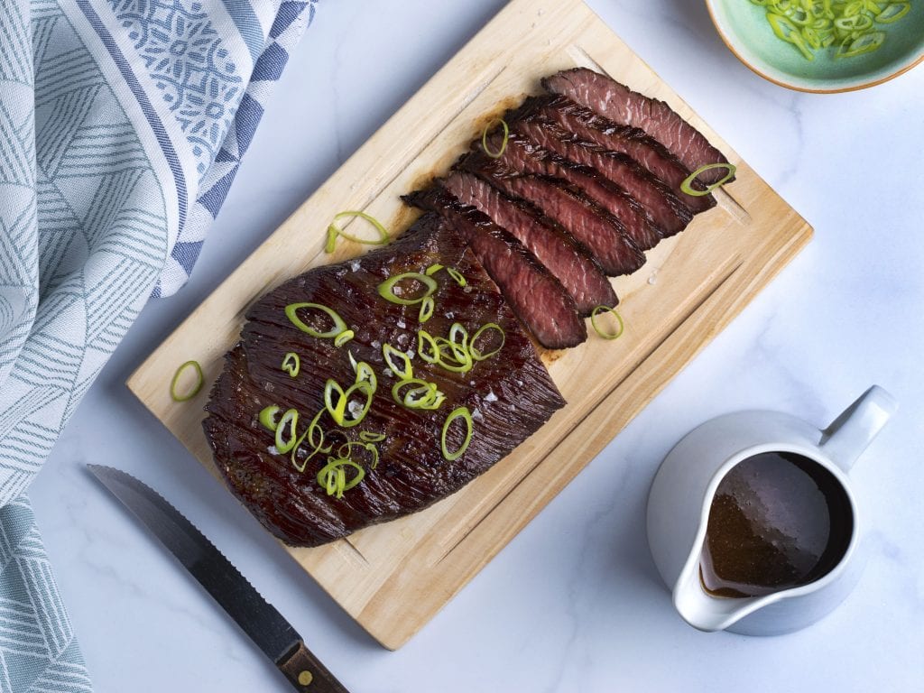flank steak with scallions on a wooden cutting board 