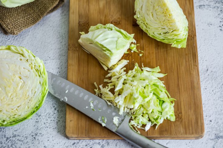 slicing green cabbage on a wooden cutting board with a chef's knife