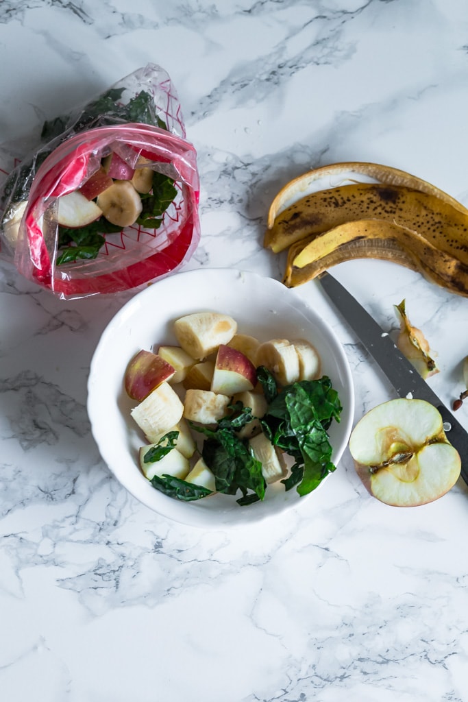 filling a bowl with kale, bananas and apples for frozen smoothies