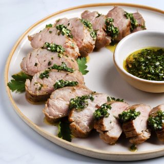 sous vide pork tenderloin sliced on a white platter with green herb sauce