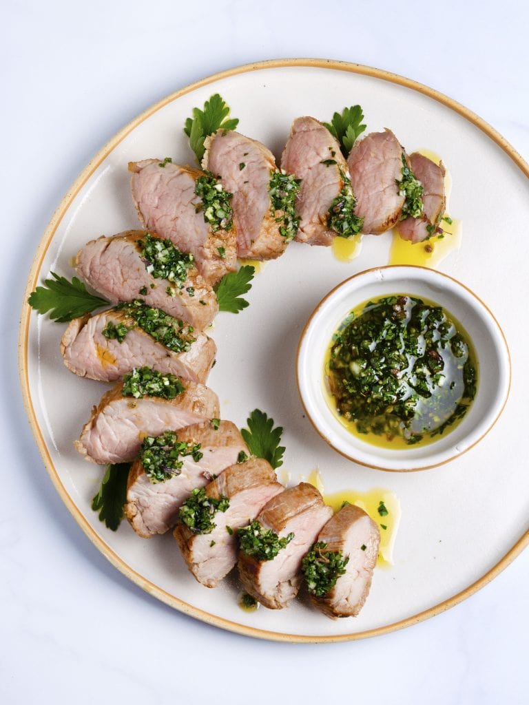 sous vide pork tenderloin sliced on a white platter with green herb sauce