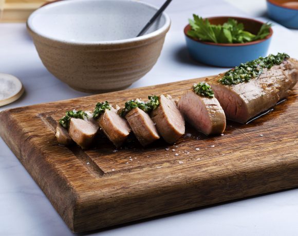sous vide pork tenderloin sliced on a wooden cutting board with green herb sauce