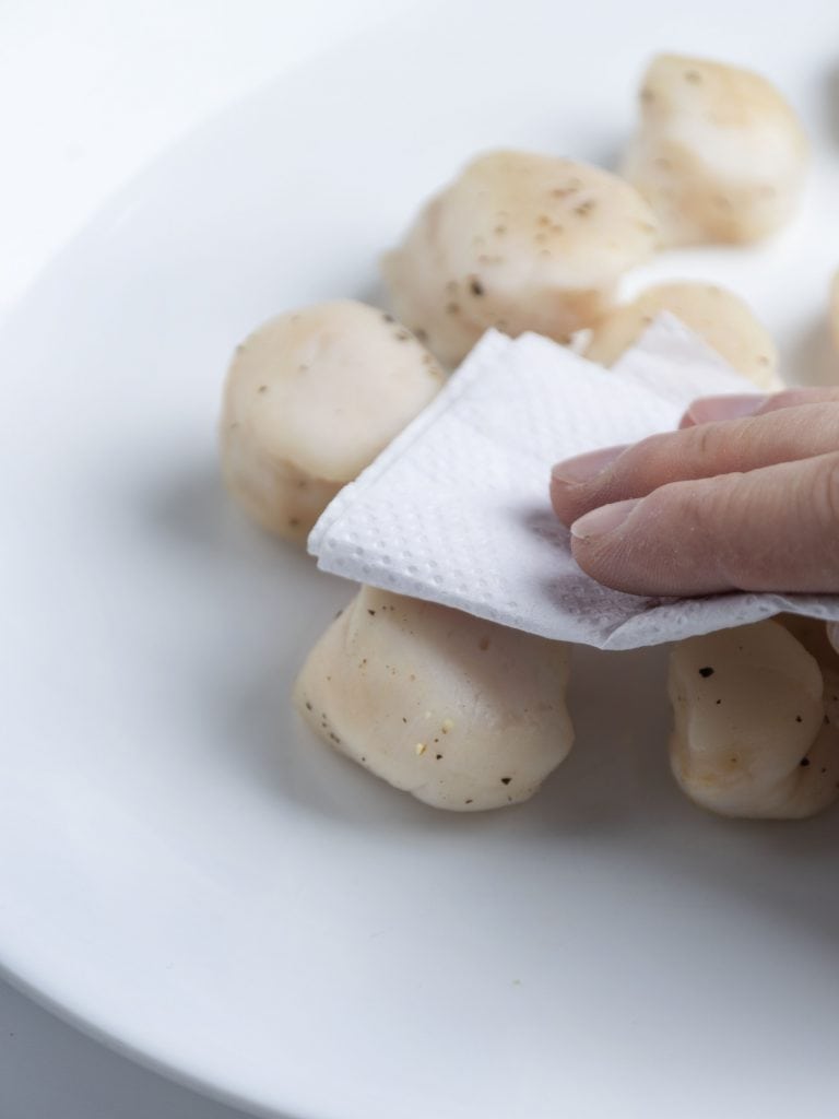 patting raw scallops dry with a paper towel