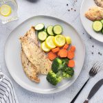 Instant pot tilapia with vegetables on a white plate with forks and knives
