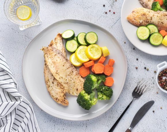 Instant pot tilapia with vegetables on a white plate with forks and knives